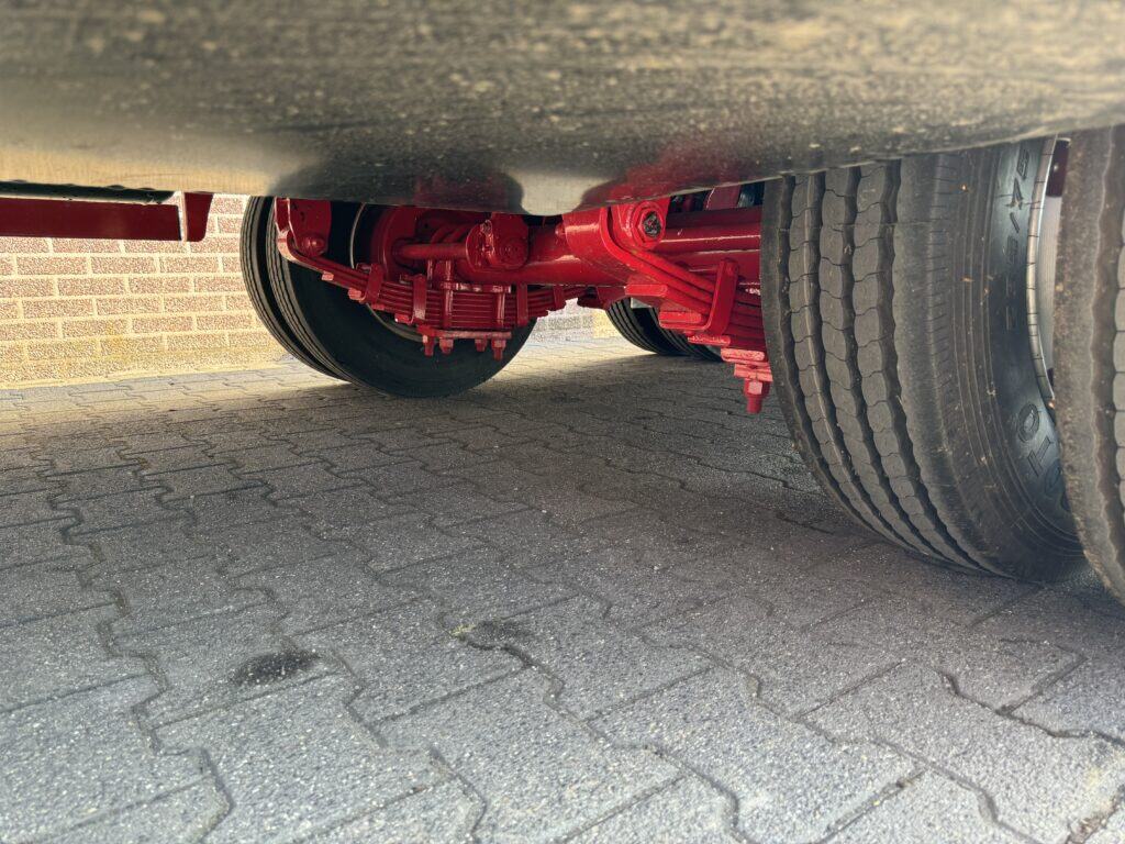 Onderkant van een vrachtwagen met rode componenten en grote banden, geparkeerd op stenen bestrating.