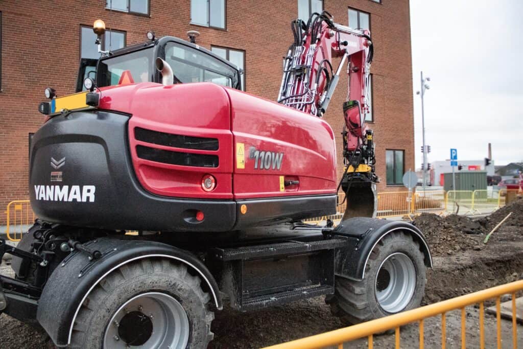 Zwaargebouwde graafmachine op bouwplaats met stedelijke achtergrond en bouwborging.