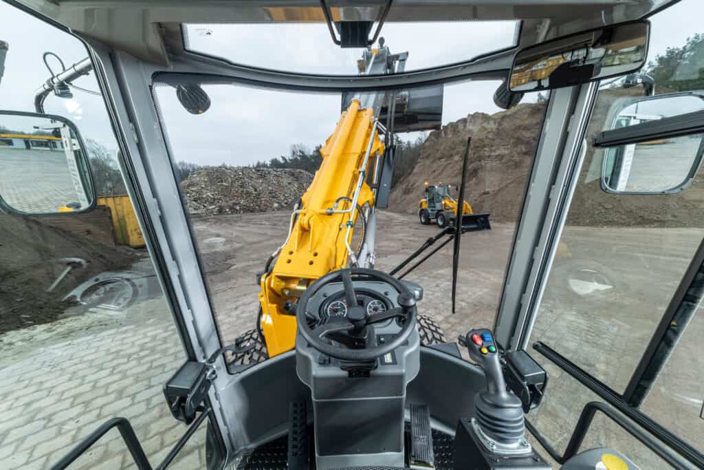 Kranbediening in een bouwvoertuig op een bouwplaats, gericht op hijsen en tillen van materialen.