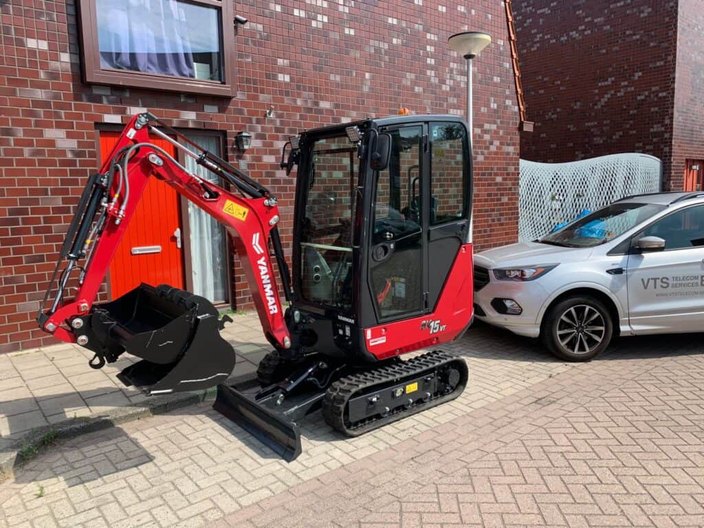 Kleine minikraan op parkeerplaats naast een auto, geschikt voor bouw- en tuinwerkzaamheden, duurzaam en wendbaar.