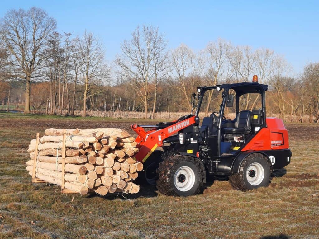 Klein shoveltreur met gestapelde houtblokken op een grasveld in de natuur.