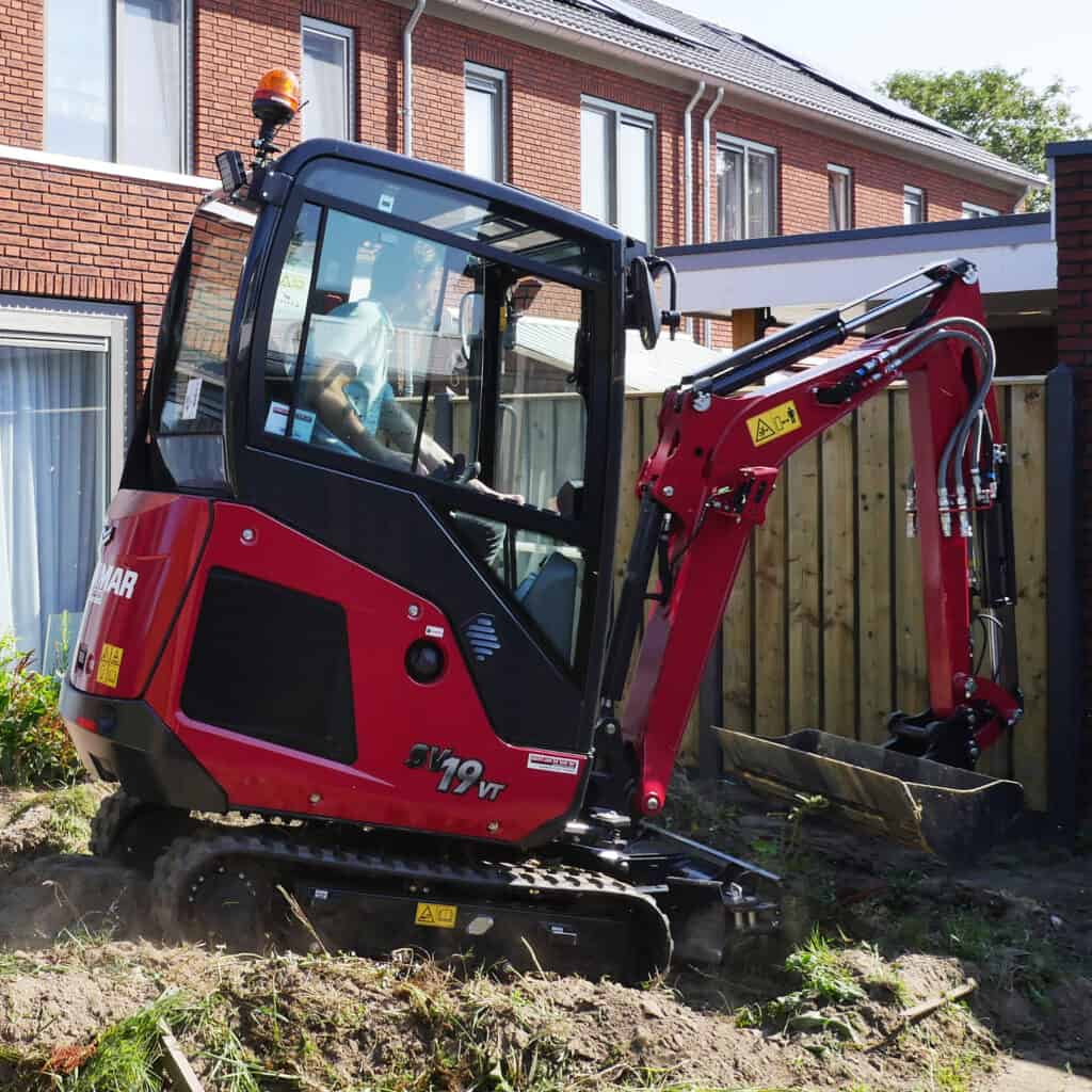 Kleine graafmachine op tuinproject bij woning, werkzaamheden in volle gang.