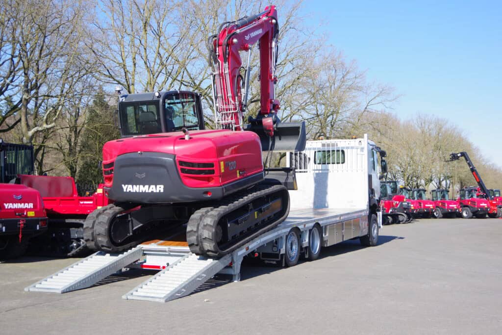 Kleine graafmachine op transportwagen op een buitenterrein met meerdere vergelijkbare machines.