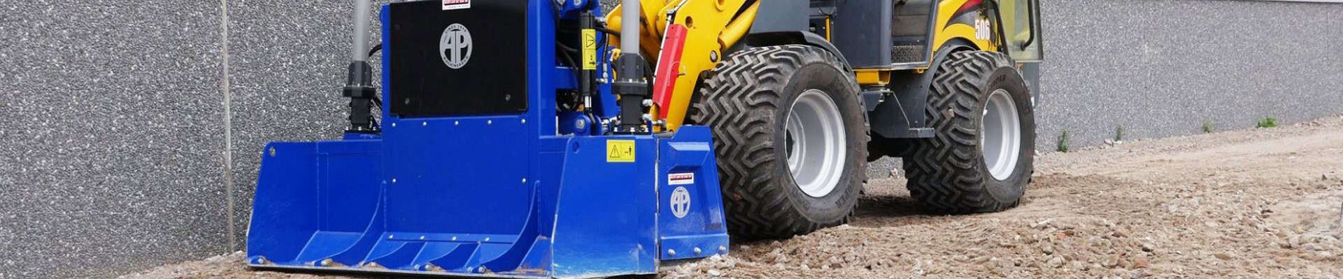 Straatbouwmachine met blauwe mengbak en grote wielen op ruw terrein.