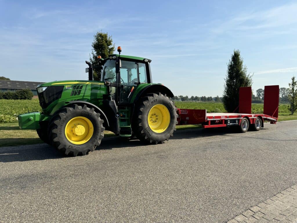 Zwarte en groene tractor met rode transportwagen op het platteland.