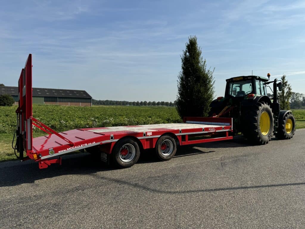 Efficiënt landbouwvervoer met een rode trekker-oplegger aan een tractor op het platteland.