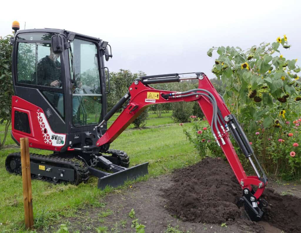 Mini graafmachine in tuin voor grondbewerking en landscaping.