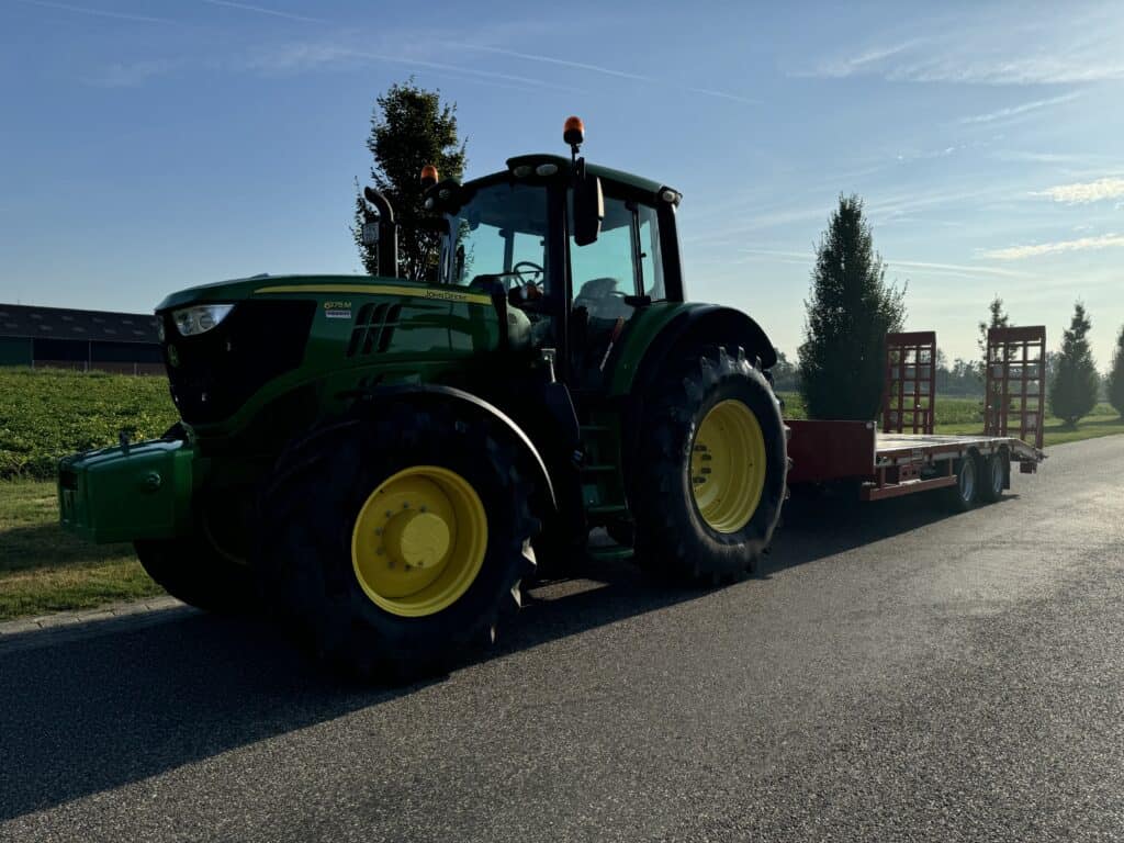 Groene landbouwtractor met aanhangwagen op landelijke weg, geschikt voor modern landgebruik.