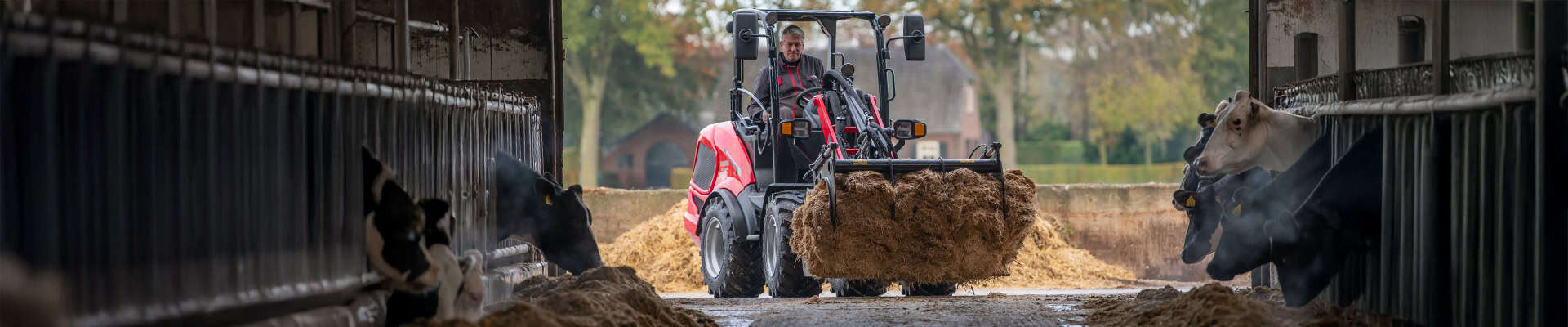 Robuuste tractor op boerderij met stro, omringd door melkkoeien in stal, voor agrarische werkzaamheden en voedselproductie.