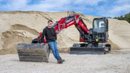 Mannelijke werknemer naast compacte graafmachine bij zandheuvels op bouwplaats.