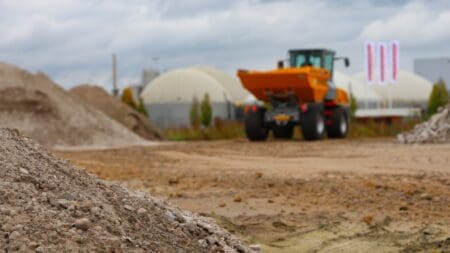 Korte omschrijving van de bouwplaats met bulldozer en bouwmaterialen in de achtergrond.