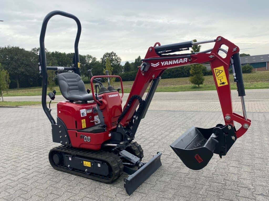 Mini kraan Yanmar SV08 op betonterrein met groene achtergronden.