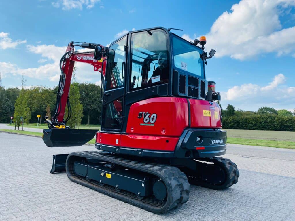 Kleine geavanceerde minigraver op oprit met groene omgeving en blauwe lucht.