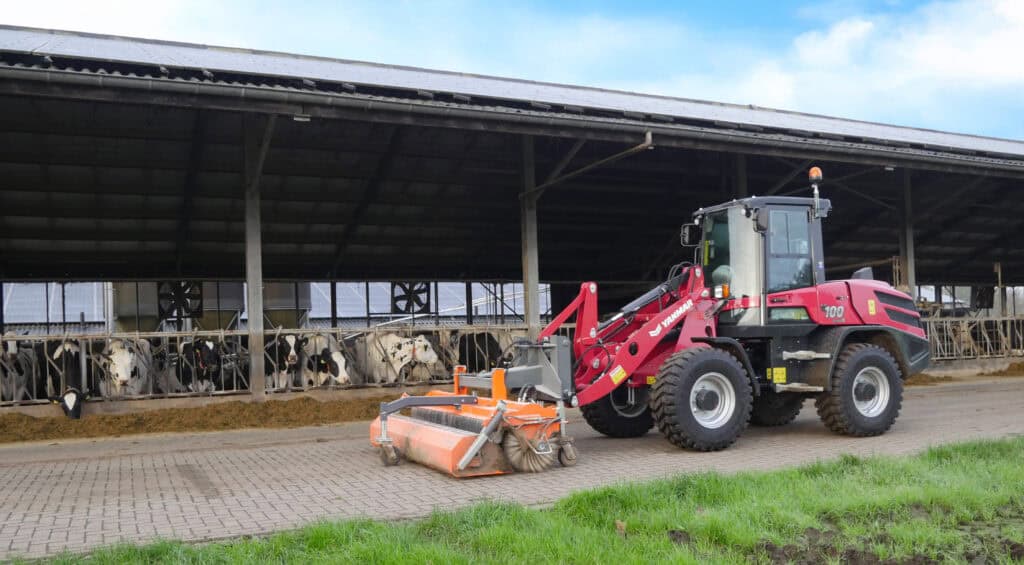 Stofzuiger voor kalverhokken op boerderij met koeien in de achtergrond.