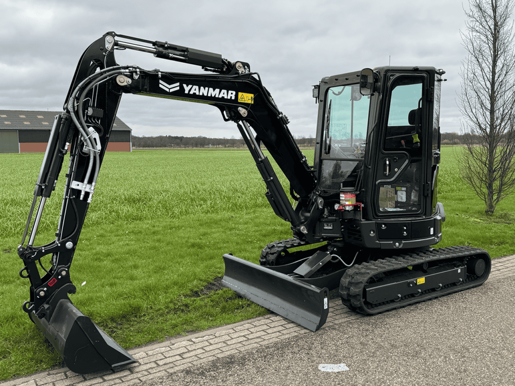Robuuste Yanmar mini graafmachine op terrein met gras en wolkenlucht.