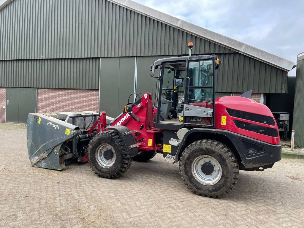 Klepelaar met voorlader, geschikt voor grondbewerking en straatvegen, op een erf voor industriële doeleinden.