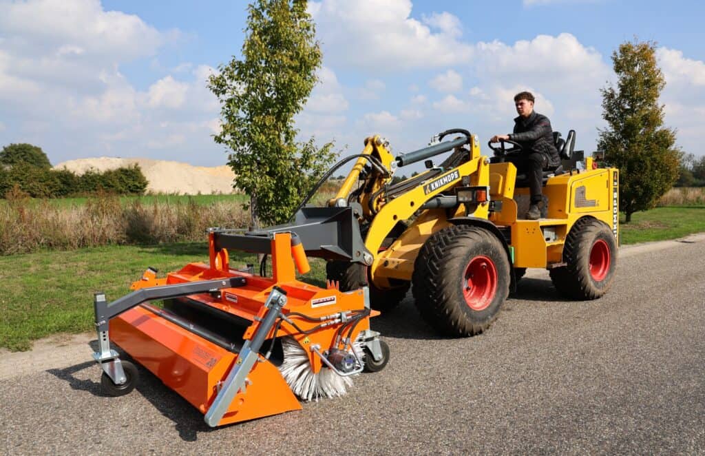 Veegmachine op een gele knikmops tractor, ideaal voor onderhoud en reiniging van wegen en terreinen.