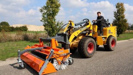 Veegmachine op een gele knikmops tractor, ideaal voor onderhoud en reiniging van wegen en terreinen.
