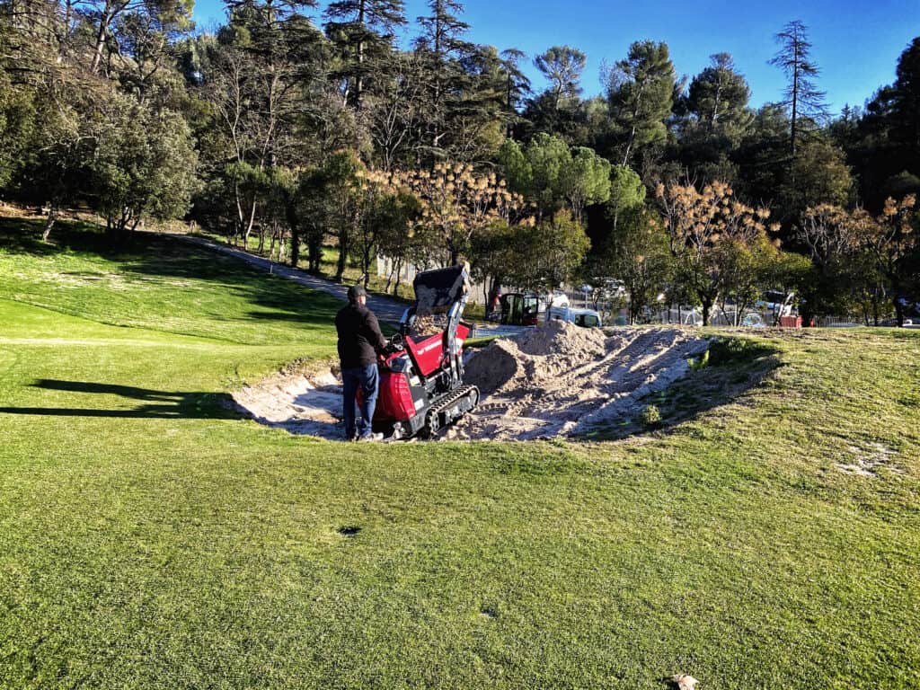 Bagger op golfbaan voor onderhoud en zandaanvoer, professionals in gras- en terreinbeheer.