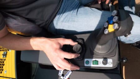 Flexibele graafmachine bediening met joystick en bedieningsknoppen op bouwmachine.