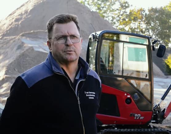 Rooie en zwarte minikraan vh bouwbedrijf Geert-Jan de Kok B.V. op bouwplaats.