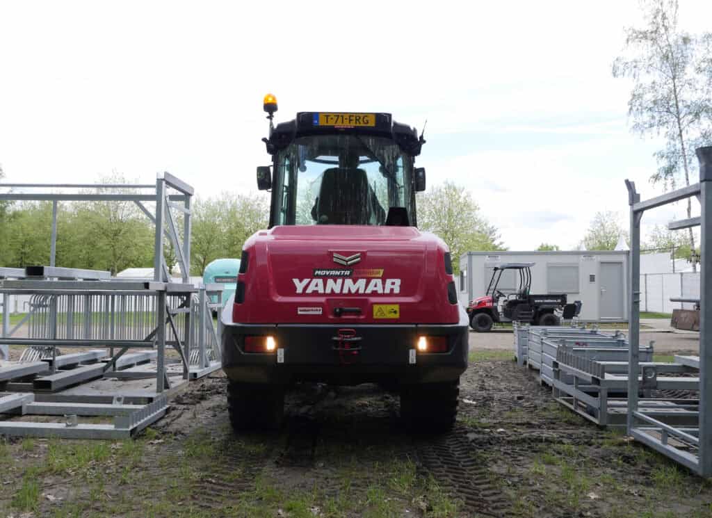 Zware Yanmar graafmachine op bouwplaats met stellingen en tuintractoren op de achtergrond.